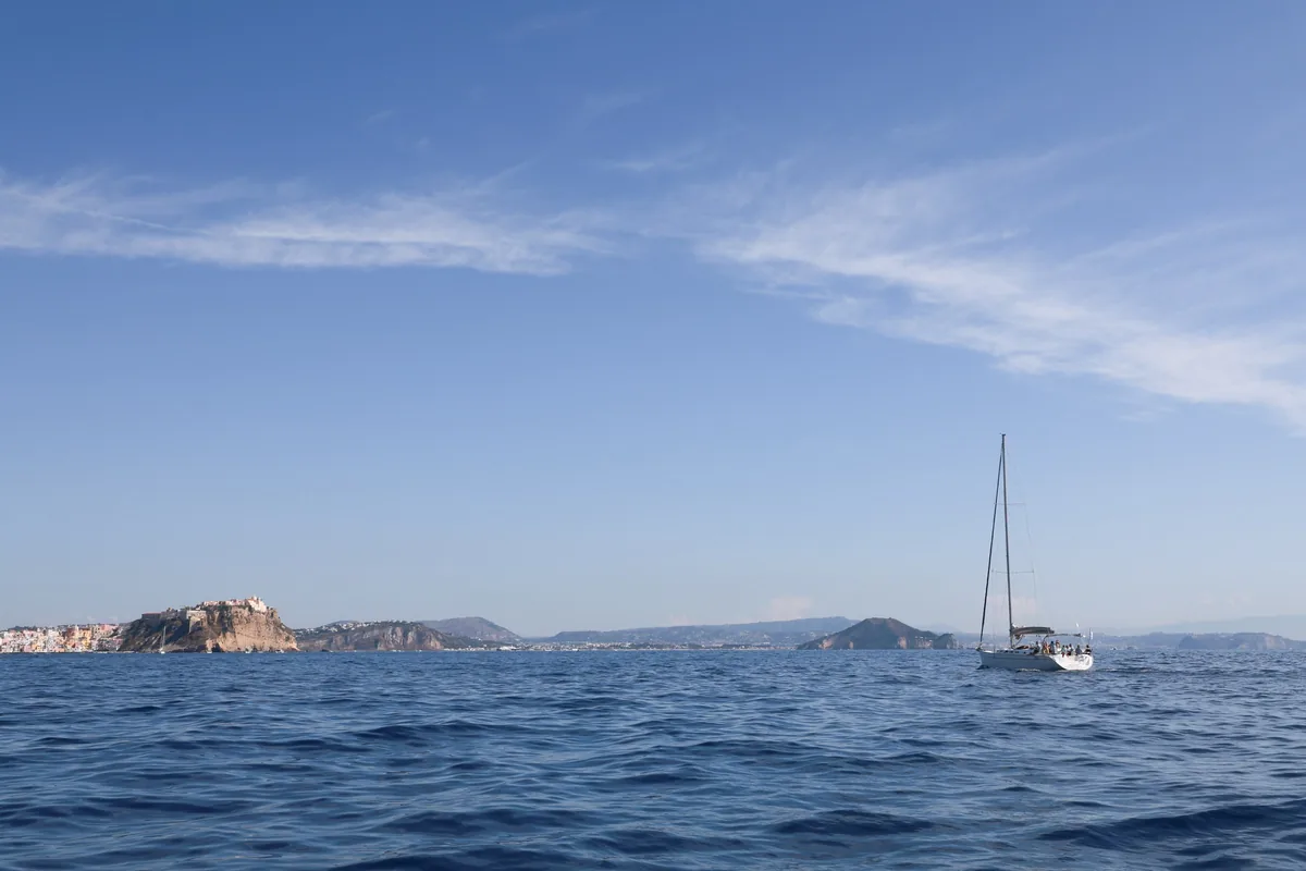 A sailing boat under way in the Gulf of Naples, with Procida and the Terra Murata in the background
